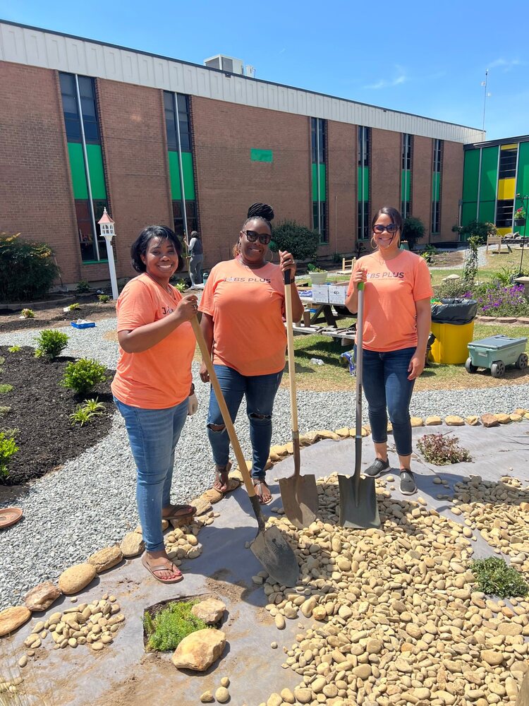 Jobs Plus staff in orange shirts are standing with their shovels in the garden outside of Carver Heights Elementary school.