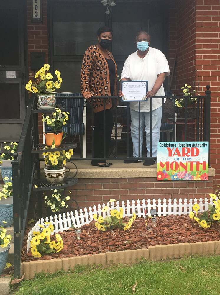 Peggy Bryant Yard of the Month Winner outside her residence holding a certificate